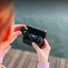 A person is holding a black charging case with a DJI microphone transmitter inside, preparing to place it into the case. Náhled obrázku produktu