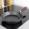 A cast iron frying pan sits on a black induction stovetop, with jars of pasta and grains in the background. Produktbild-Vorschau