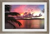 A framed picture of a tropical sunset over the ocean, with a palm frond in the foreground. Produktbild-Vorschau