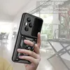 A hand holding a black phone case with a ring holder and slide camera cover, with a blurred interior background. Produktbild-Vorschau