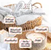 A basket filled with white towels, with several decorative labels placed around it, and a lit candle in a decorative holder in the foreground. Produktbild-Vorschau
