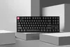 A black mechanical keyboard with a pink keycap is displayed on a white pedestal against a backdrop of geometric shapes. Produktbild-Vorschau