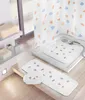 A bathroom scene featuring a shower curtain, shower mat, and bath mat with a seashell pattern. Produktbild-Vorschau