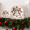 Christmas-themed tableware with snowman designs, displayed on a shelf with a garland. Voir les images du produit