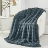 A dark gray plush blanket draped over a white chair next to a white cabinet with a lamp and a vase. Produktbild-Vorschau