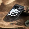 A black phone case with a white ring is partially buried in sand, with a piece of wood and a rock nearby. Anteprima dell’immagine prodotto