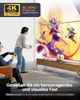 Two people are playing video games in a living room, with a large TV displaying a colorful game. Produktbild-Vorschau