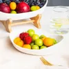 A close-up of a fruit bowl with various fruits, including strawberries, grapes, and oranges, on a white surface with a glass of water in the background. Produktbild-Vorschau