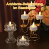 A decorative display of LED tealights in a multi-tiered gold candelabra and glass holders, with flowers in the background. Produktbild-Vorschau