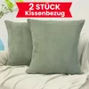 Two green corduroy pillow covers are displayed on a textured white blanket, with a hint of greenery and a blue vase in the background. Produktbild-Vorschau