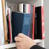 A hand reaches for a book on a shelf. Produktbild-Vorschau