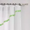 A close-up view of a white sheer curtain with green ribbon accents hanging from a curtain rod. Produktbild-Vorschau