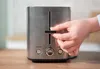 Hand zieht Krümelschublade mit Krümeln aus Unold Toaster Tom, Text: „Herausnehmbare Krümelschublade“ Produktbild-Vorschau