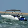 A white boat with a gray bimini top and a blue jet ski attached, floating on the water near a sandy beach. Náhľad obrázku produktu