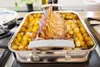 A roasted rack of lamb with potatoes in a roasting pan on a stovetop. Produktbild-Vorschau