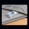 A bundle of charging cables is being placed into a laptop bag, which is resting on a wooden surface. Produktbild-Vorschau