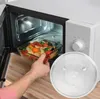 A hand is placing a glass bowl of vegetables into an open microwave. A glass turntable is also visible in the foreground. Náhľad obrázku produktu
