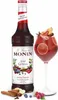 A bottle of Monin Spiced Red Berries syrup and a glass of red beverage garnished with fruit and spices. Voir les images du produit