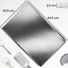 A rectangular baking tray is shown from a slightly elevated angle on a white background. Dimensions are indicated with lines and text. Other kitchen utensils like a grater and a spoon are visible in the lower part of the image. Anteprima dell’immagine prodotto