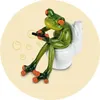 A decorative frog figurine sitting on a toilet and holding a remote control. Produktbild-Vorschau