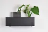 A black metal wall planter with a plant and a decorative item inside, mounted on a white wall. Produktbild-Vorschau