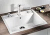 A white kitchen sink with a modern faucet and soap dispenser, set on a wooden countertop with small bowls of ingredients in the background. Produktbild-Vorschau