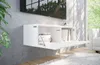 A modern white wall-mounted TV cabinet with the front panel open, revealing books inside, is shown in a well-lit room with a window and plush rug. Náhled obrázku produktu