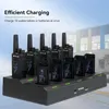 A charging station with multiple walkie-talkies and batteries plugged in, with a building in the background. Náhľad obrázku produktu
