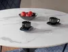 A round dining table with a marble-like finish, set with a bowl of red apples and two coffee cups and saucers. Anteprima dell’immagine prodotto