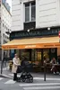 A woman pushes a stroller past a boulangerie in Paris. Produktbild-Vorschau
