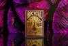 A deck of Bicycle playing cards with a peacock design is displayed on a reflective surface with a vibrant, abstract background. Produktbild-Vorschau