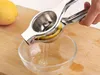 A hand squeezing a lemon in a stainless steel juicer over a glass bowl. Produktbild-Vorschau