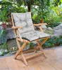 A light gray chair cushion on a wooden chair in a garden setting with a pond and plants. Voir les images du produit