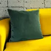 A green corduroy pillow rests on a yellow sofa in front of a textured gray wall. Produktbild-Vorschau
