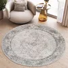 A round rug with a vintage design is placed on a wooden floor in a living room setting, next to a modern armchair and a side table. Produktbild-Vorschau