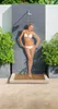 A woman in a bikini stands under an outdoor shower next to potted plants. Produktbild-Vorschau