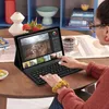 A person is using a tablet with a keyboard attached, editing photos on a wooden table. Produktbild-Vorschau