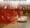 A robot vacuum cleaner is shown on a wooden floor near a dining table, with a red overlay indicating a 'no-go zone'. Produktbild-Vorschau