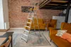 A stepladder is set up in a living room with brick walls, sofas, and a rug. Náhľad obrázku produktu