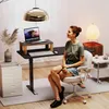 A woman is sitting at a standing desk in a home office setting. Voir les images du produit