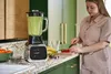 A woman is preparing ingredients for a smoothie in a modern kitchen, with a blender prominently displayed. Produktbild-Vorschau
