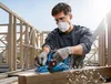 A man is using a Bosch power planer on a wooden beam at a construction site. Podgląd zdjęcia produktu