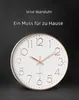 A close-up of a wall clock with text overlays. Produktbild-Vorschau