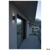 A modern balcony with a view of a town and mountains at dusk, featuring wall-mounted lights. Produktbild-Vorschau