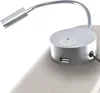 A close-up of a silver bedside lamp with a USB port and a switch, attached to a beige upholstered headboard. Náhled obrázku produktu