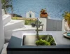 A modern kitchen sink with vegetables, set against a backdrop of a white staircase, a bell tower, and the blue sea. Podgląd zdjęcia produktu
