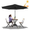 A young girl sits at a small table under a large black umbrella, with two chairs and a potted plant on the table. Voir les images du produit