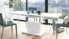A modern dining set with a white extendable table and teal chairs, set in a bright room with a mountain view. Produktbild-Vorschau