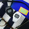 Two Casio Baby-G watches, one black and one white, are placed on a striped fabric next to a blue notebook with a yellow "TRAVEL NOTES" sticker. Produktbild-Vorschau