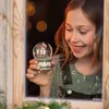 A young girl looks at a snow globe through a window. Produktbild-Vorschau